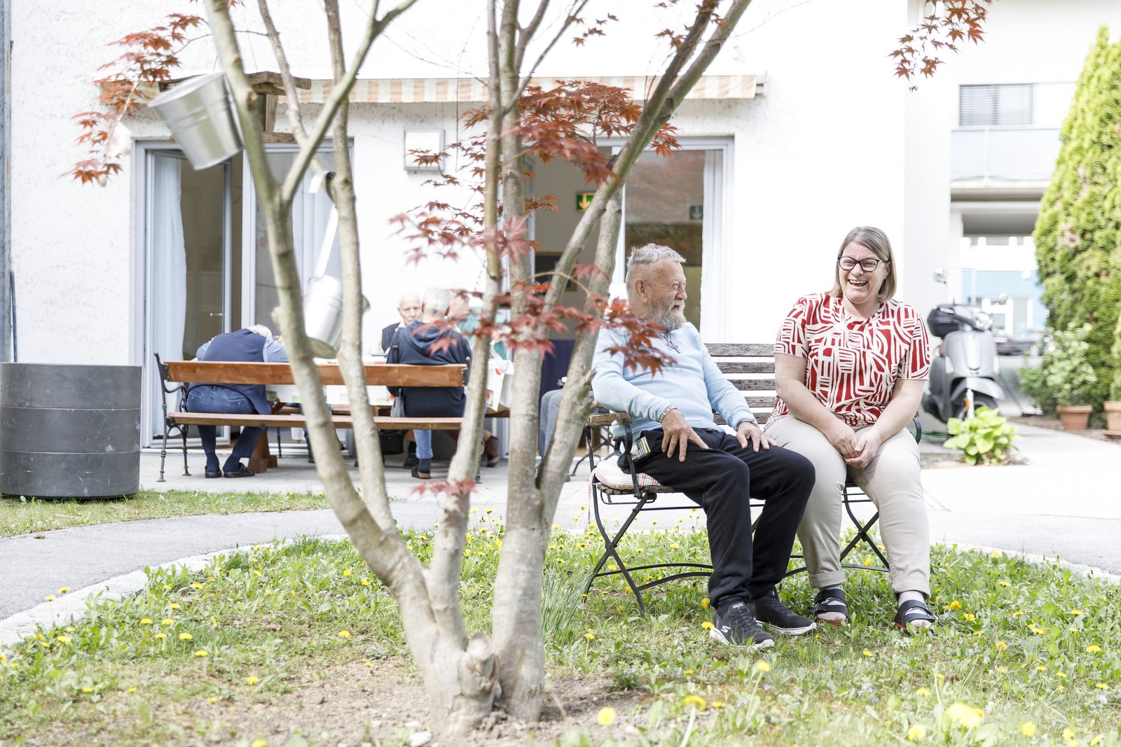 Eine Pflegeperson spricht mit einem Gast, draußen im Garten