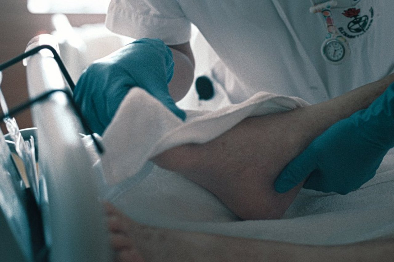Eine Pflegekraft mit blauen Handschuhen wäscht den Fuß von einer Patient:in mit einem weißen Tuch.