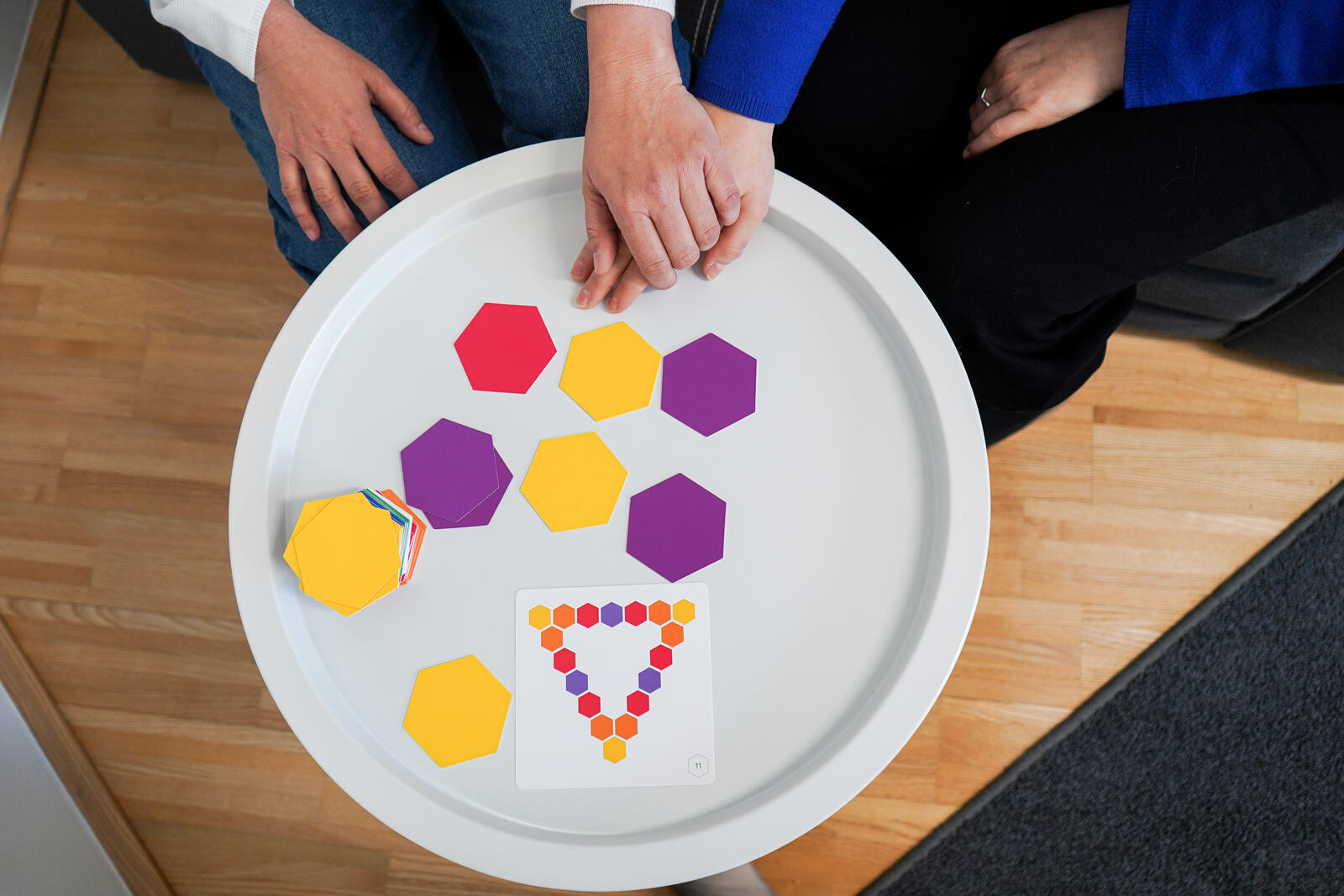 Eine Hand führt eine andere zu einem Tisch mit bunten Spielkärtchen (Gedächtnisspiel)