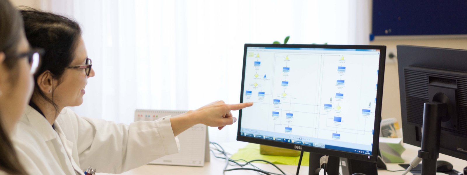 Zwei Mitarbeiter:innen sitzen im Büro vor einem Monitor und analysieren gemeinsam ein Diagramm.