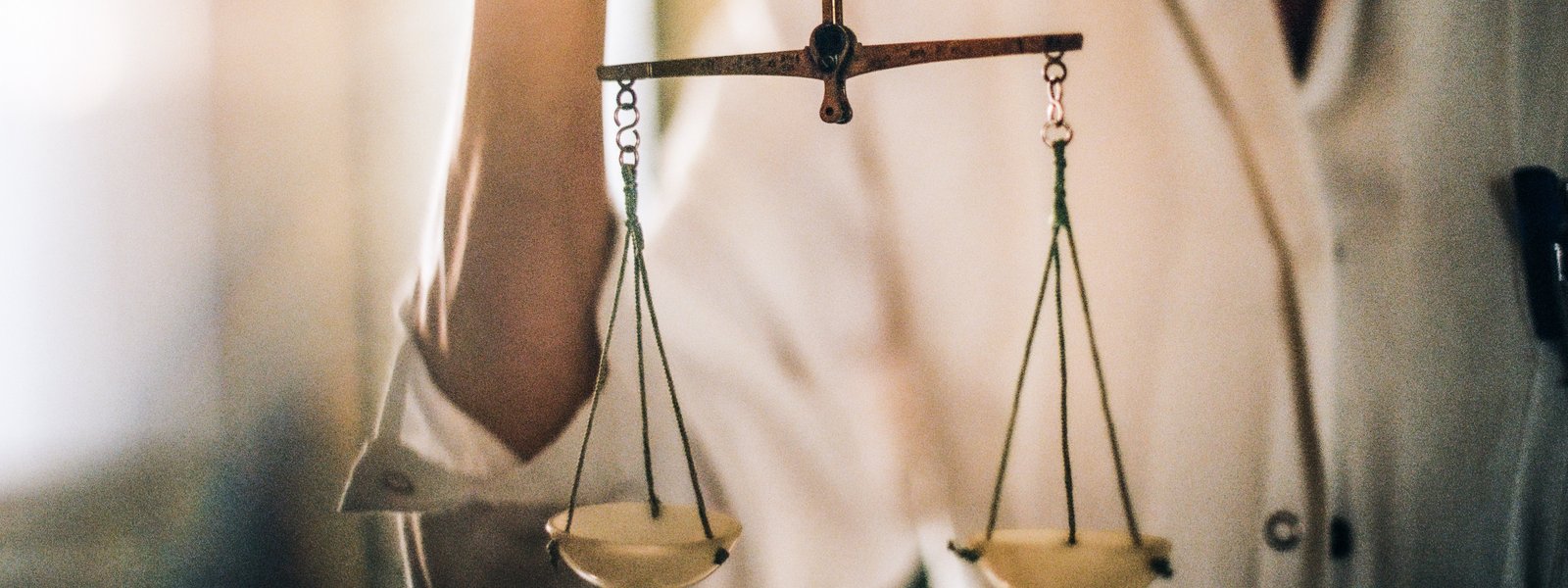 Altmodische Waagschale, die eine Apotheker:in in weißem Kittel hält.