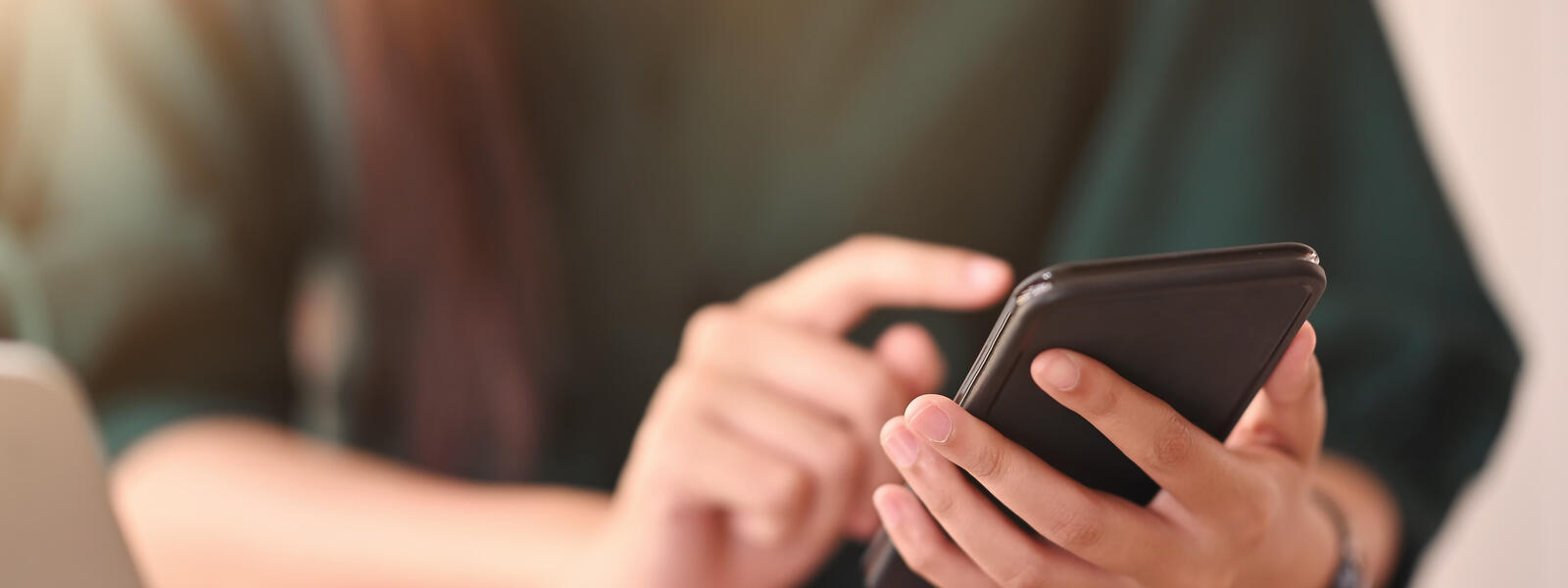 Person mit grünem T-Shirt und Smartphone in der Hand