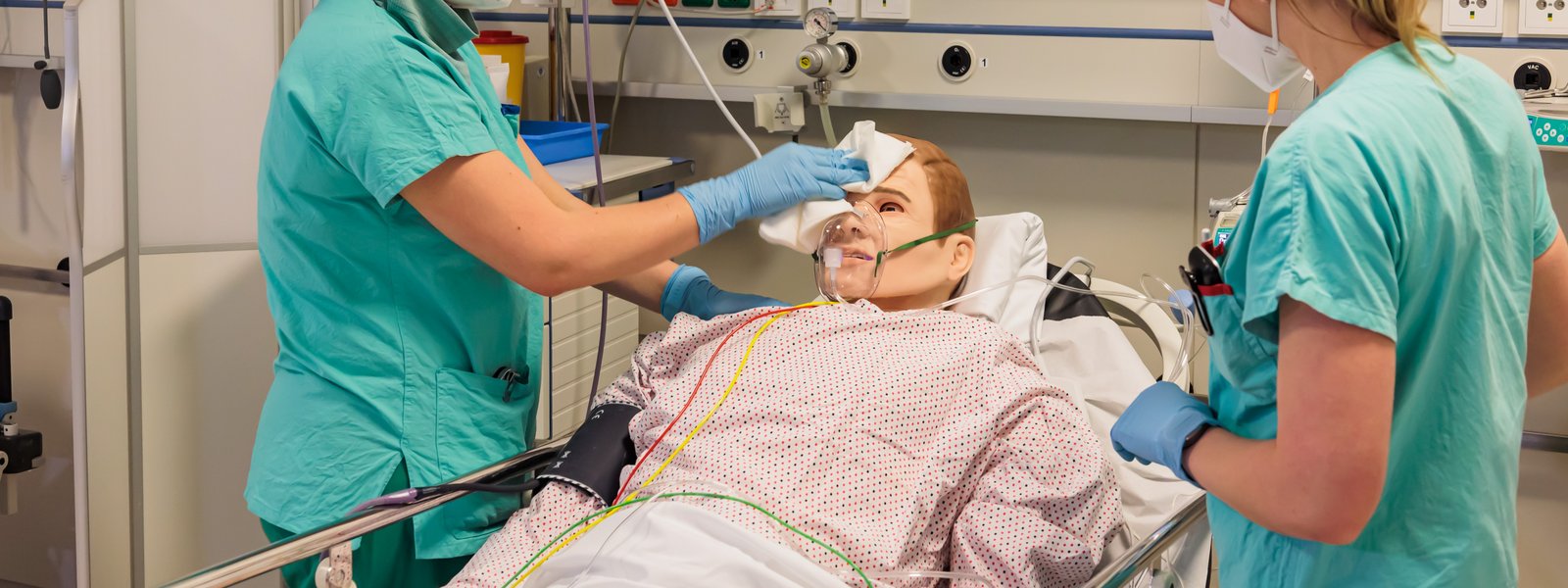 Zwei Pflegepersonen die an einem Patientensimulator stehen.