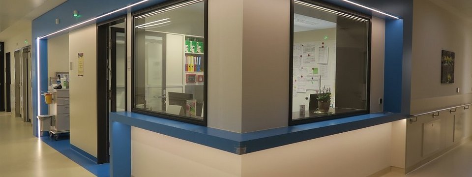 Stützpunkt einer der innenmedizinischer Stationen mit moderner blauer Wand und langen Gang zu den Patient*innenzimmern.