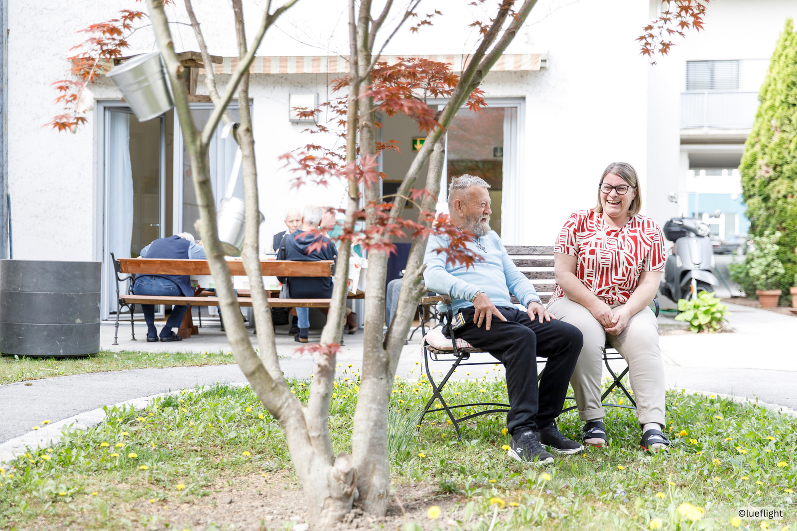 Eine Pflegeperson spricht mit einem Gast, draußen im Garten