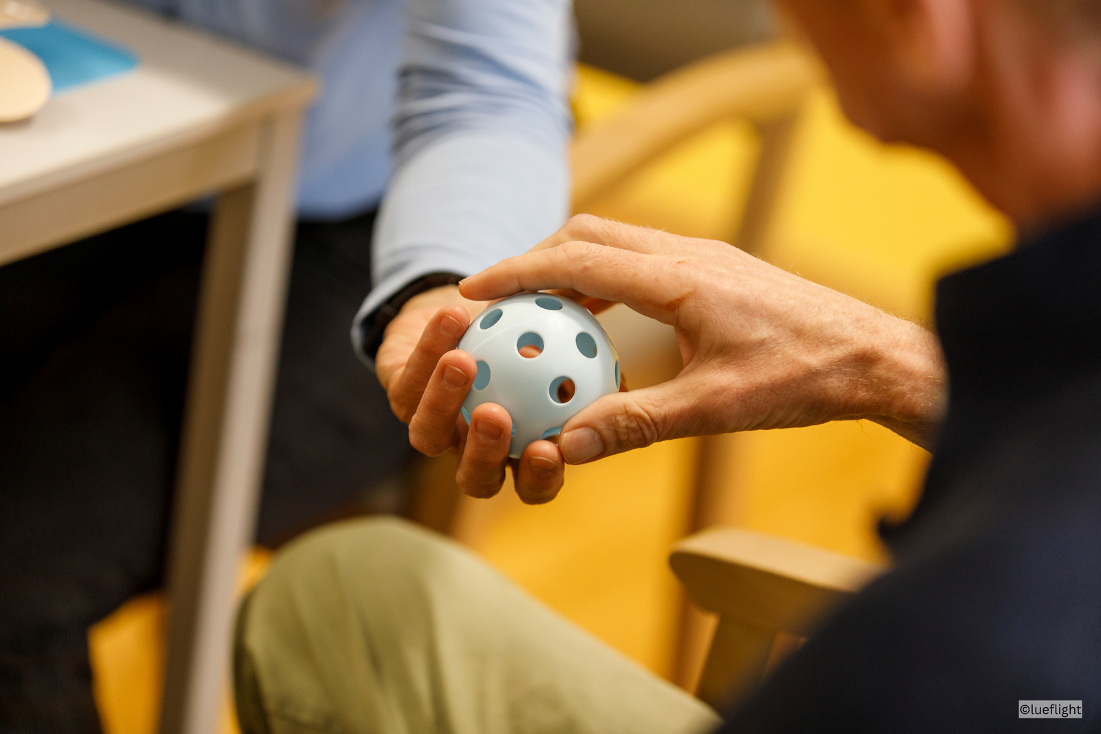 Eine Betreuungsperson gibt einem Gast einen Ball um die Motorik zu trainieren