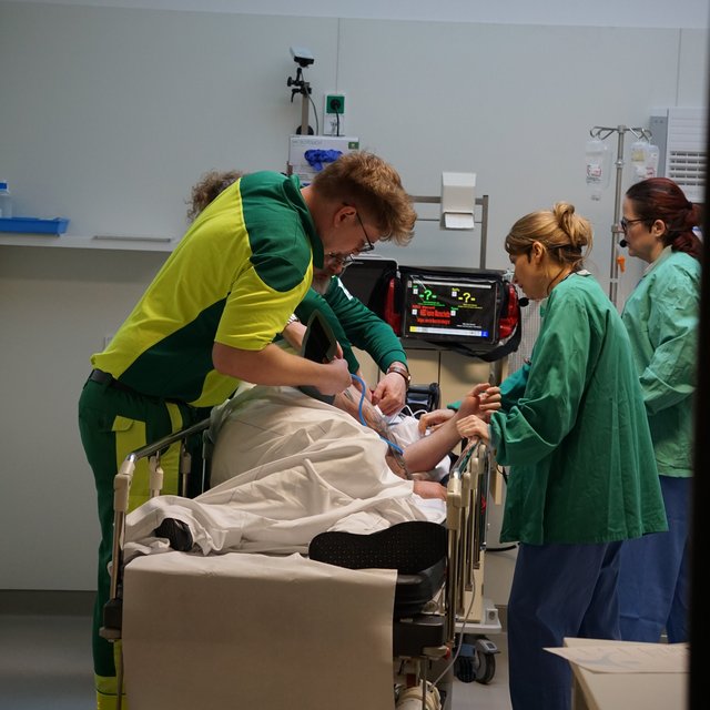 Simulationstraining, Medizinisches Personal versorgt Patient:in auf einer Liege in der Notaufnahme.
