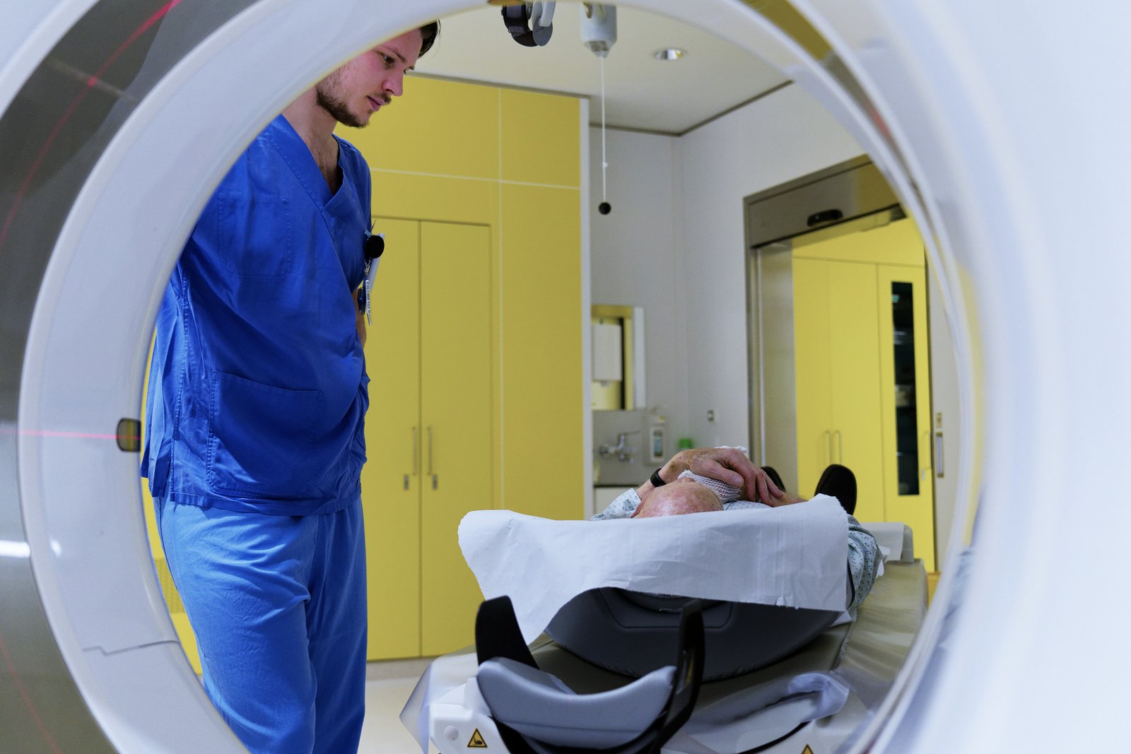Ein Radiologe vor dem CT Gerät, auf der Liege ein:e Patient:in
