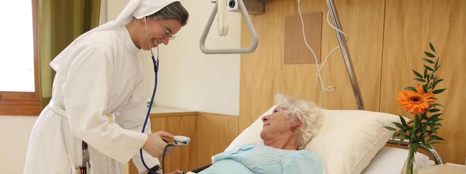 Eine Schwester mit Stethoskop, die eine Frau damit abhört.